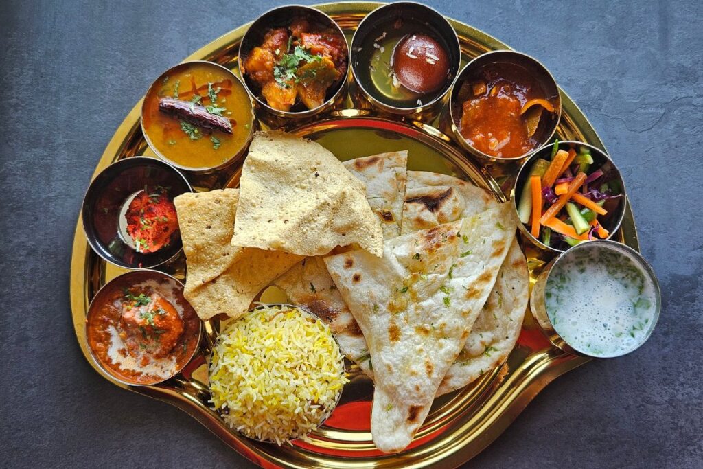 Colorful Indian thali with curries, naan, rice, and assorted accompaniments.