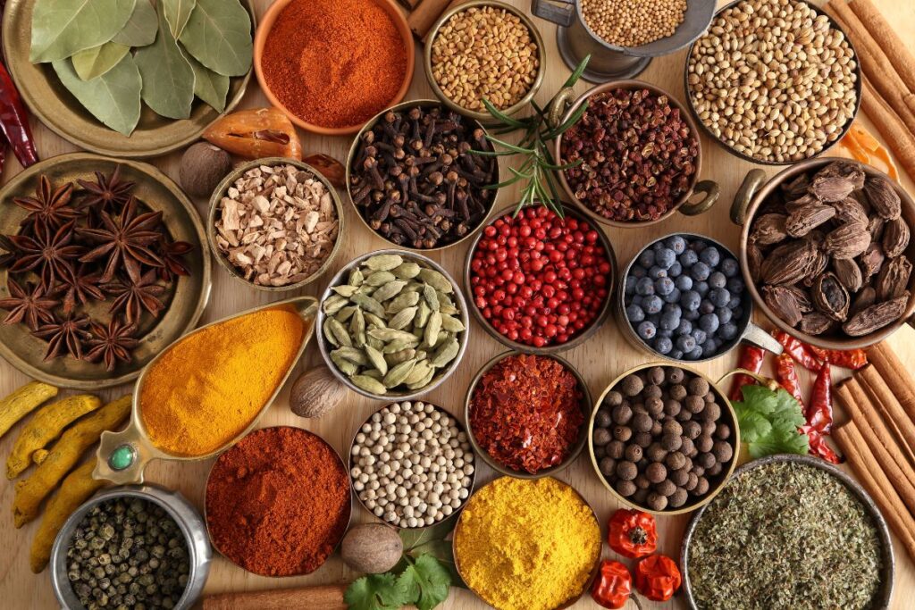 Flat lay of colorful Indian spices in small bowls, including turmeric, cardamom, and chili.