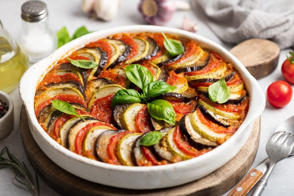 Rustic vegetable ratatouille arranged in a round baking dish with fresh basil leaves.