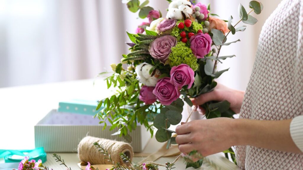 Person arranging a bouquet and removing extra leaves before placing flowers in a vase.