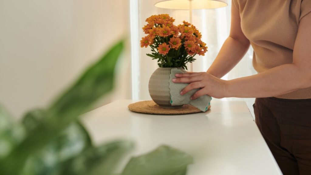 Person cleaning a ceramic vase before arranging orange flowers on a tidy table.