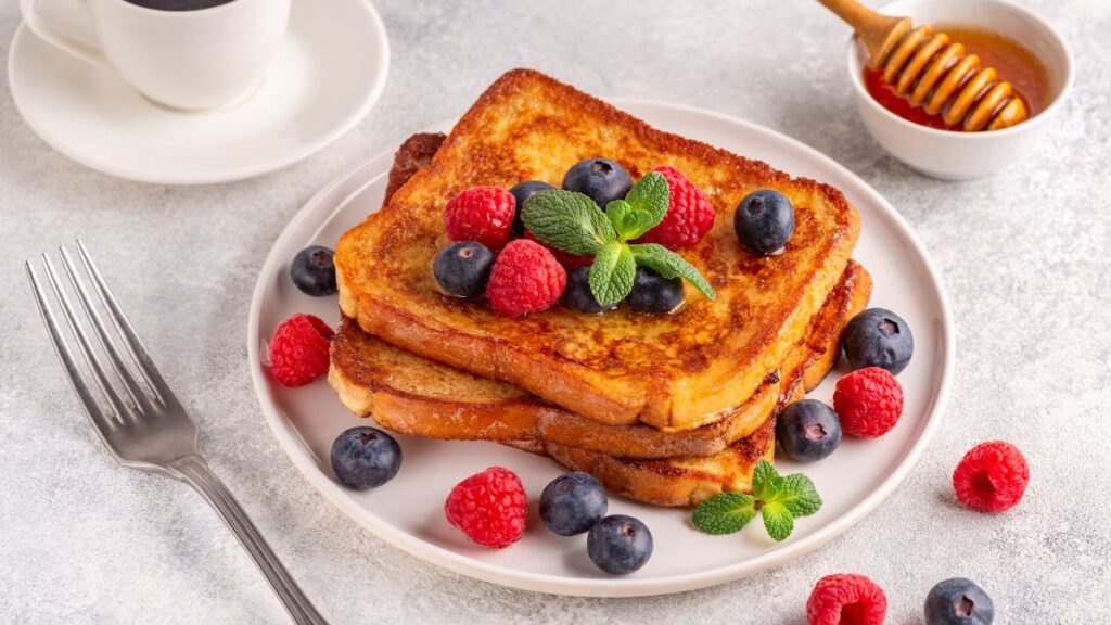 Stack of French toast topped with fresh berries and mint on a white plate.