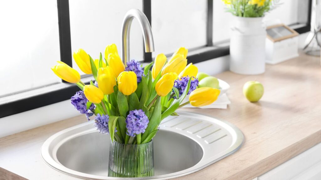 Bright yellow tulips and purple hyacinths soaking in fresh water in a kitchen sink.