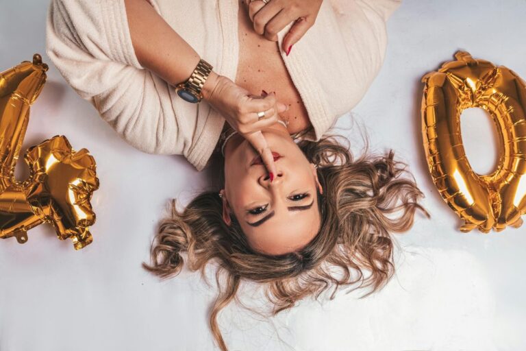 Confident woman turning 40 lying on the floor with gold birthday balloons and a playful expression.
