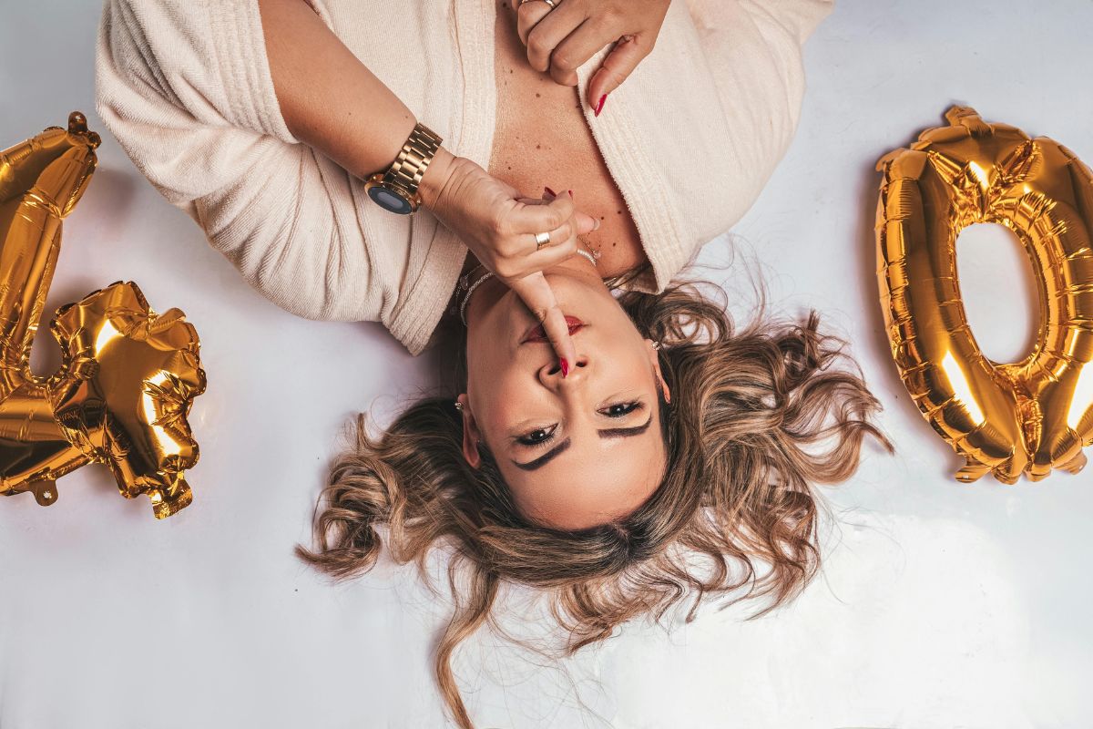 Confident woman turning 40 lying on the floor with gold birthday balloons and a playful expression.