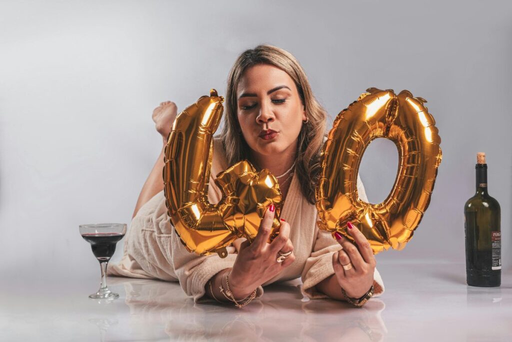 Playful 40th birthday celebration with woman kissing gold balloons and sipping red wine.