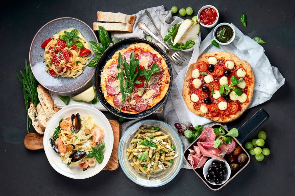 Italian table spread with pasta, pizza, and antipasti served with fresh bread.