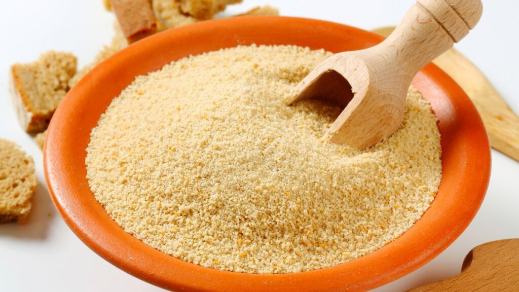 Bowl filled with golden breadcrumbs and a wooden scoop on a kitchen counter.