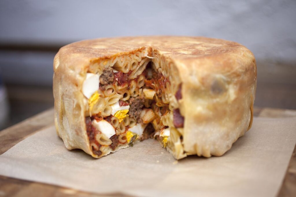 Baked pasta timballo sliced open to reveal layers of noodles, eggs, and sauce.