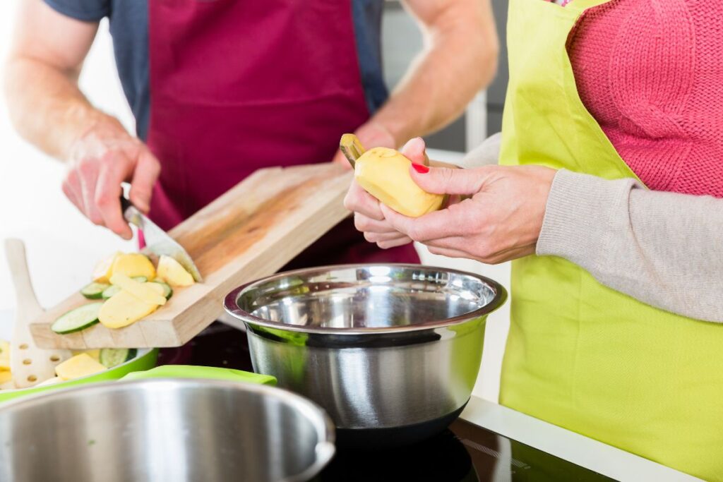 Couple preparing vegetables together in a kitchen, slicing squash and zucchini.