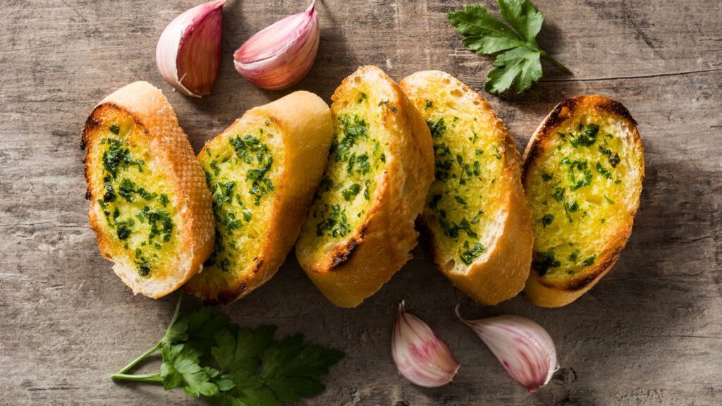 Slices of toasted garlic bread with herbs and fresh parsley on a rustic wooden surface.