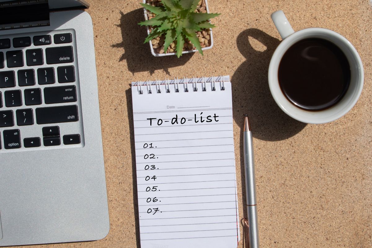 Open to-do list with laptop, coffee, and pen on desk.