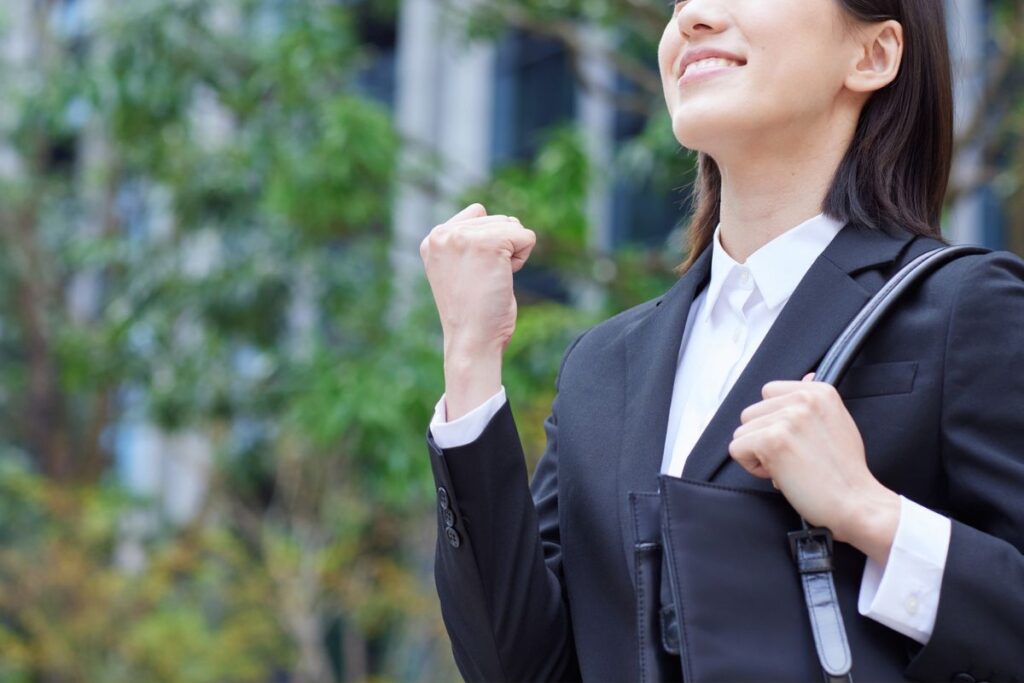 Businesswoman smiling with fist raised in celebration outdoors.