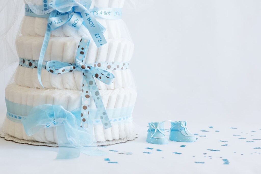 Blue ribbon diaper cake decorated with baby shoes and confetti on a white background.
