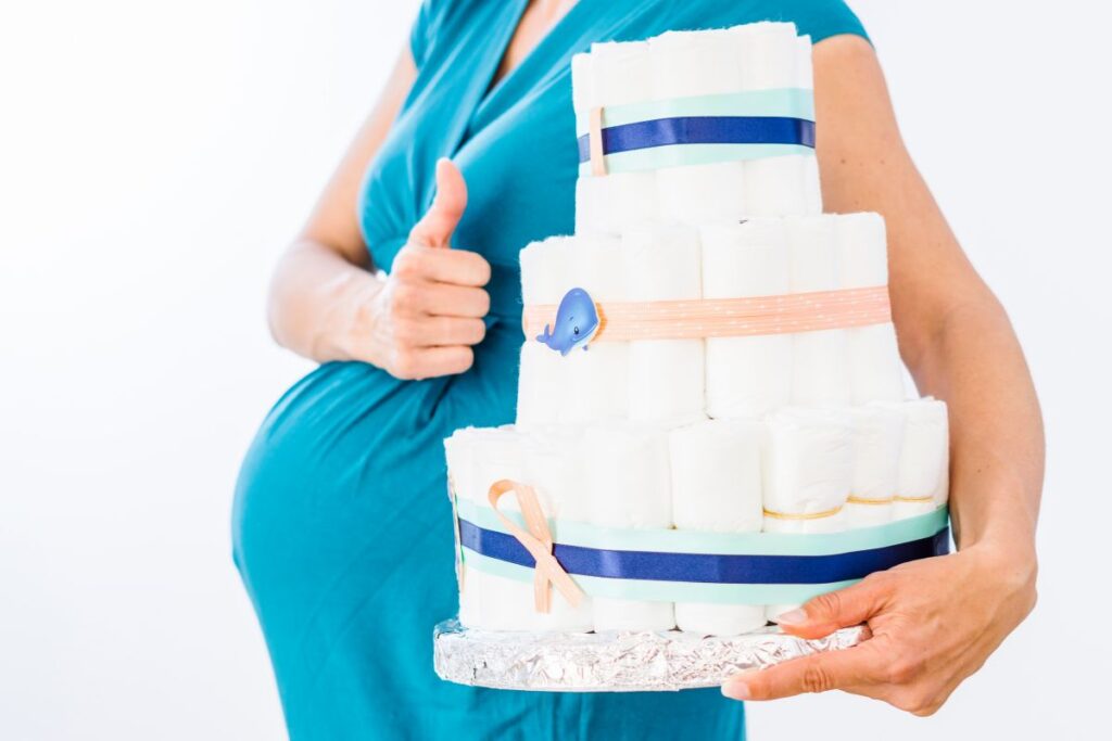 Person in a teal dress holding a large diaper cake decorated with ribbons.