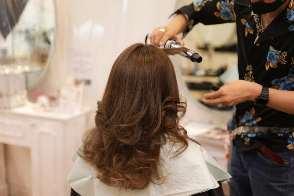 Hairstylist curling soft layered hair in a salon, representing modern hairstyles for women over 50.