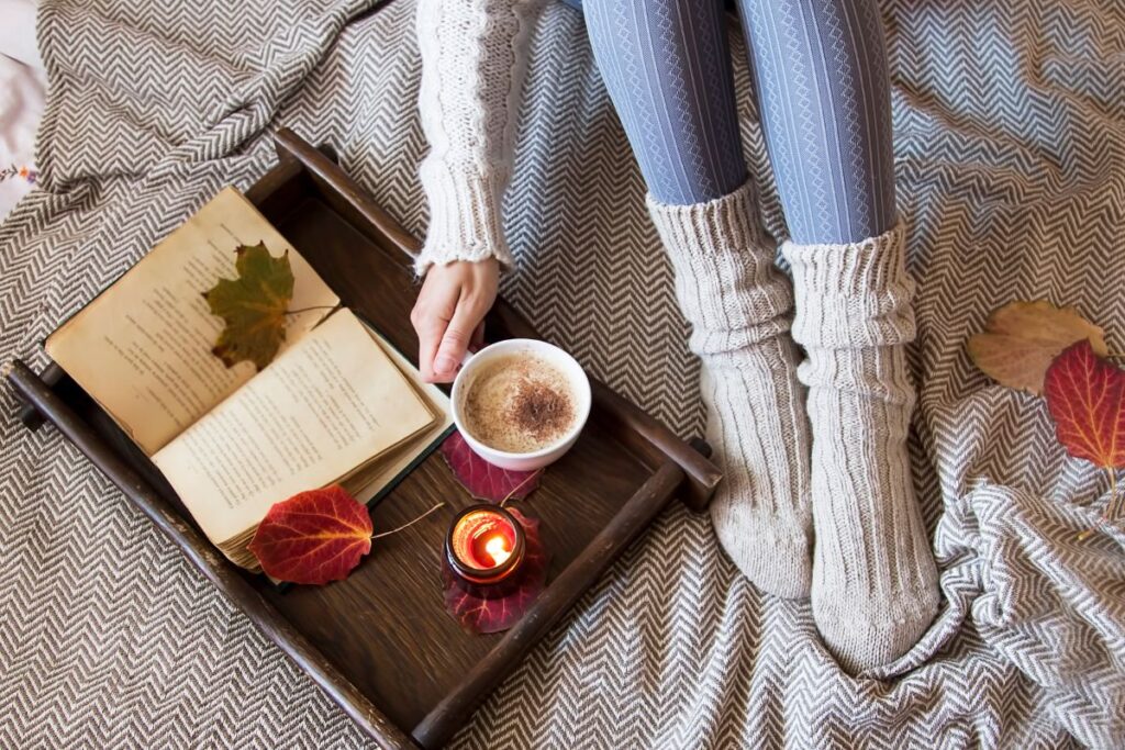 Warm cozy scene with coffee, book, and candle on a tray with knitted socks.