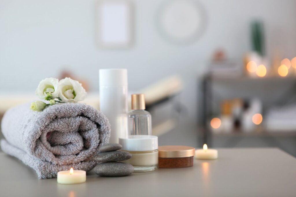 Soft spa scene with rolled towel, candles, and skincare jars in gentle light.
