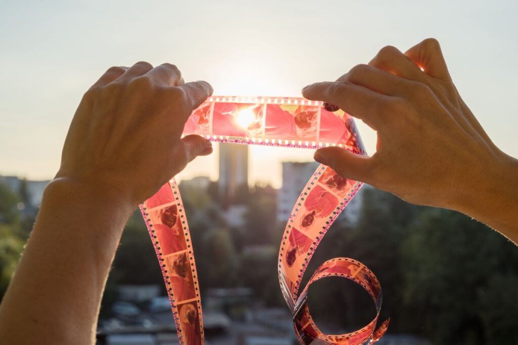 Hands holding film negatives up to sunlight with blurred city view behind.