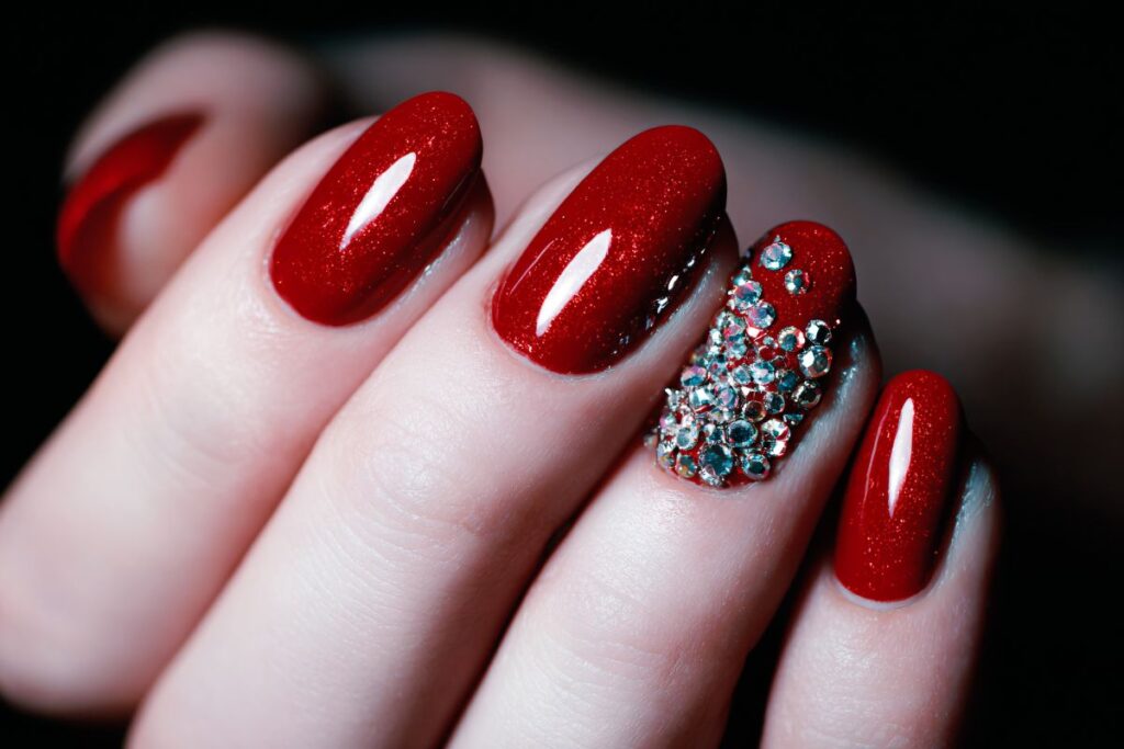 Red glitter nails with rhinestone accent for holiday manicure.