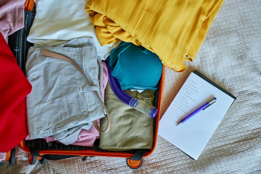 Open suitcase with colorful winter clothes and a packing checklist for a winter travel wardrobe for women over 50.