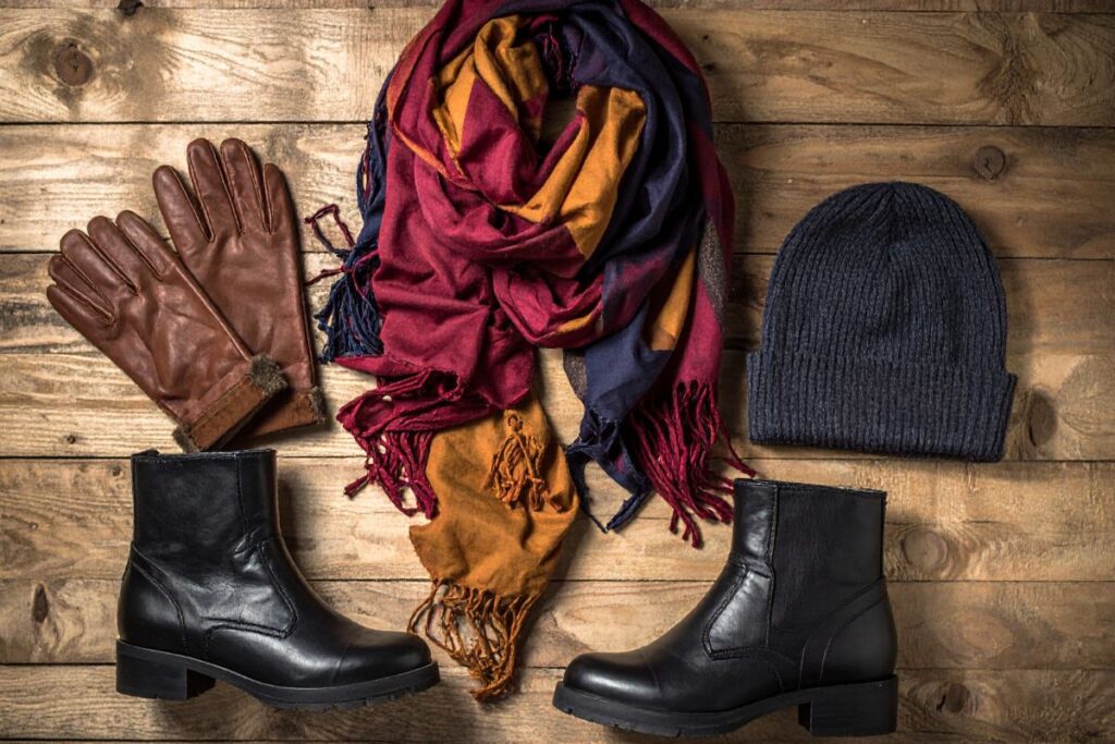 Winter accessories flat lay with leather gloves, scarf, hat, and boots for stylish cold-weather travel outfits.