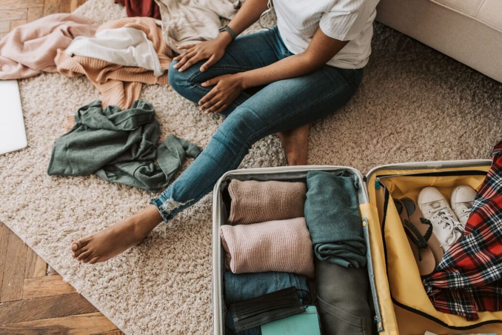 Woman packing folded sweaters, jeans, and shoes into suitcase as part of a casual winter travel wardrobe.