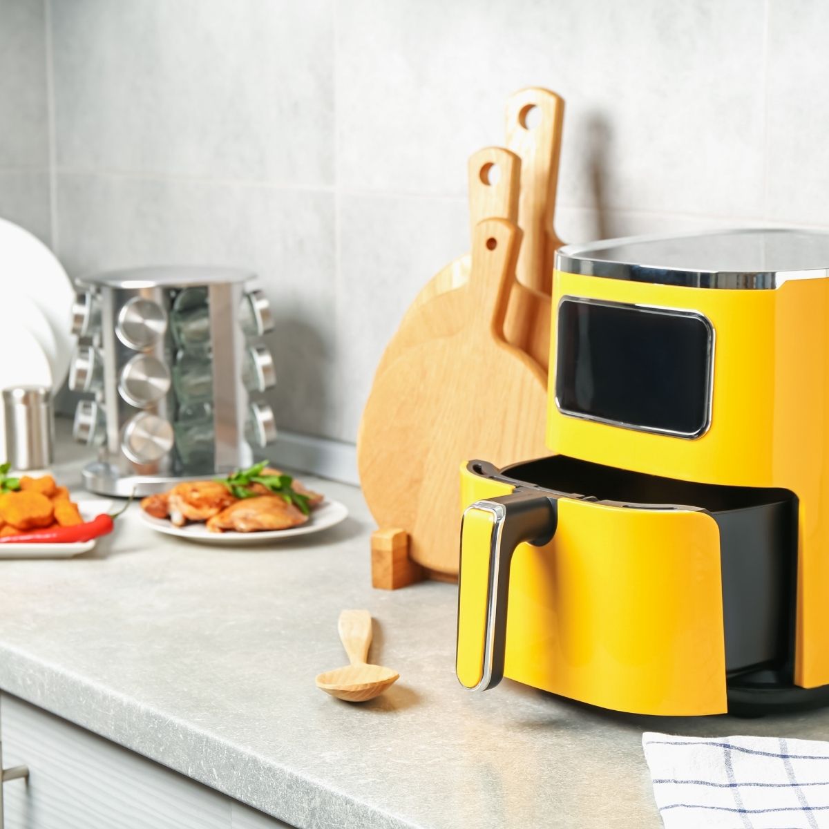 Bright yellow air fryer on a kitchen counter next to wooden cutting boards.