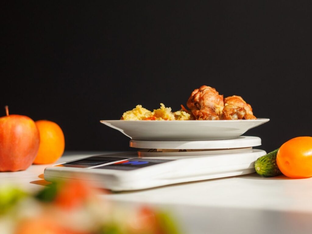A plate of chicken and mashed potatoes is being weighed on a white digital kitchen scale.