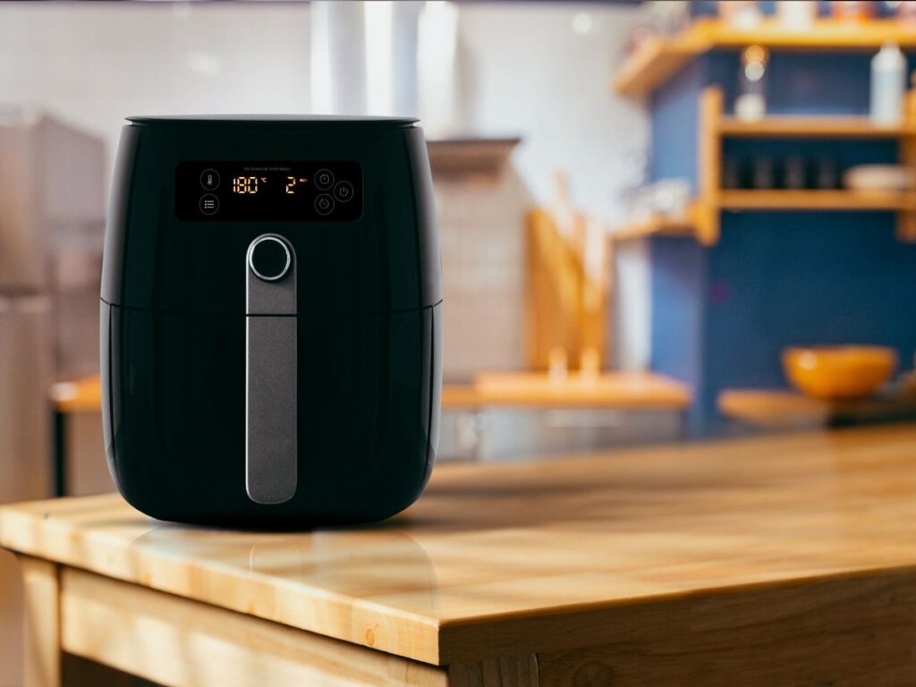 Black digital air fryer sitting on a wooden kitchen countertop.