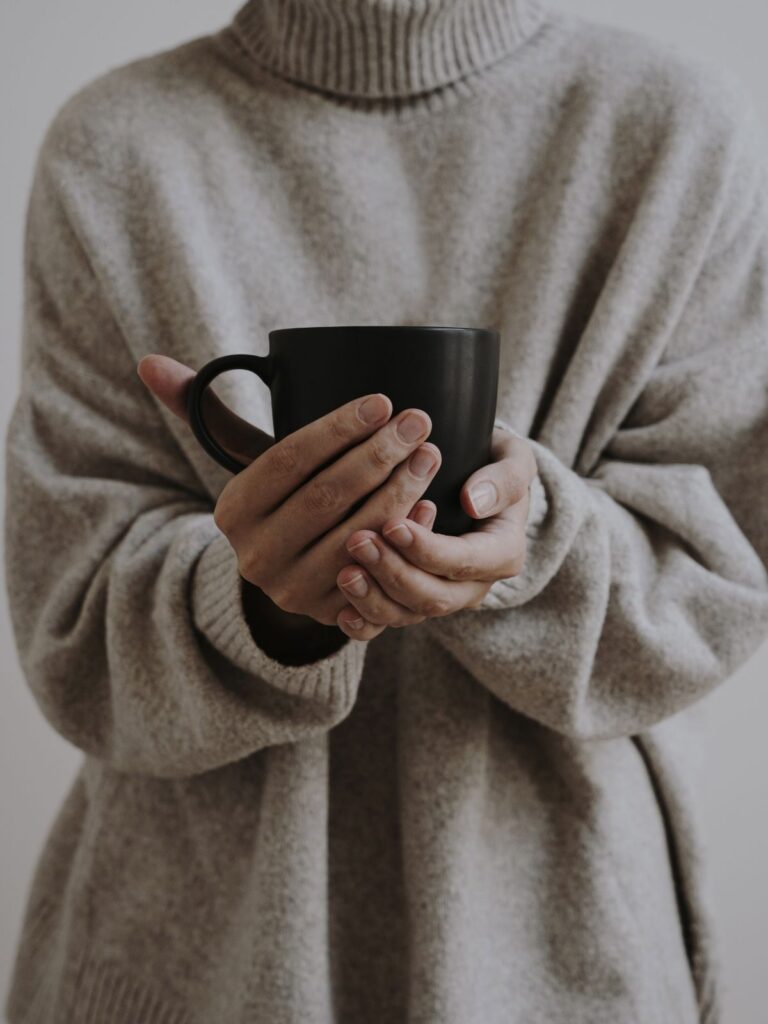 Woman wearing pullover outfit and holding a coffee mug.