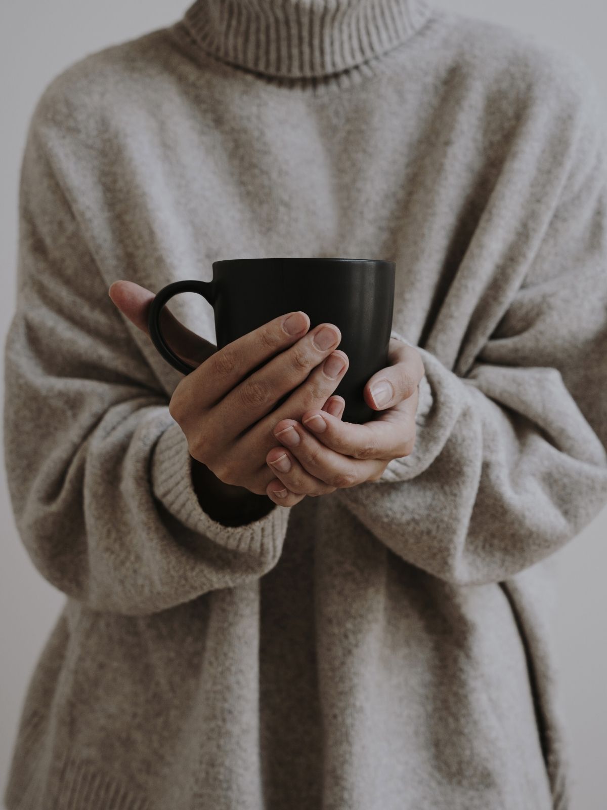 Woman wearing pullover outfit and holding a coffee mug.