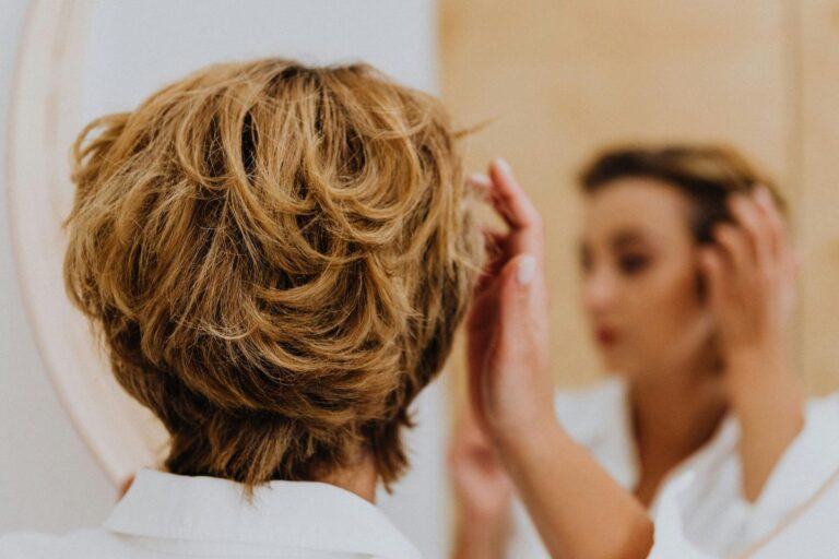 A mature woman styling wavy hair in front of a mirror.