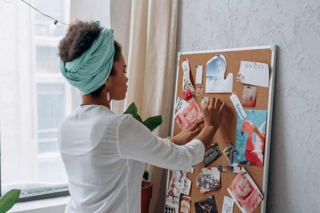 Woman arranging printed images on a vision board in a calm, bright space.