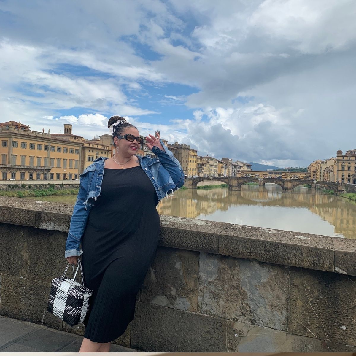 Woman in denim jacket posing on a bridge over a river in a European city