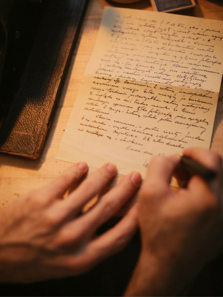Hands writing a handwritten letter at a wooden desk in warm light.