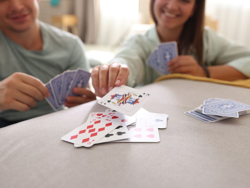 A smiling couple sitting together on a couch, playing a card game and placing cards onto a small pile on a table
