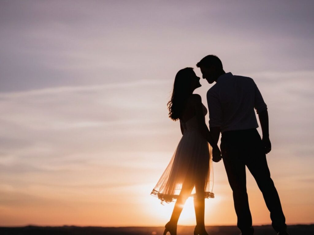 Silhouette of a couple holding hands and leaning close at sunset.