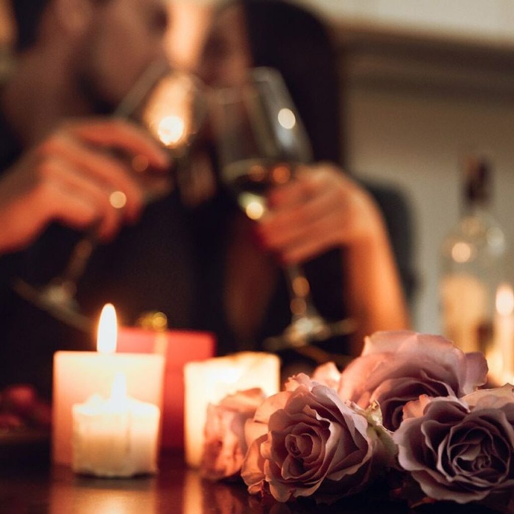 Romantic candlelit dinner setup with wine glasses and roses in the foreground.