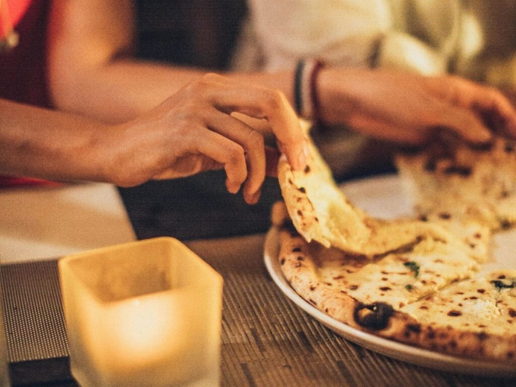 A couple enjoying a cozy candlelit meal, sharing slices of pizza at the table.
