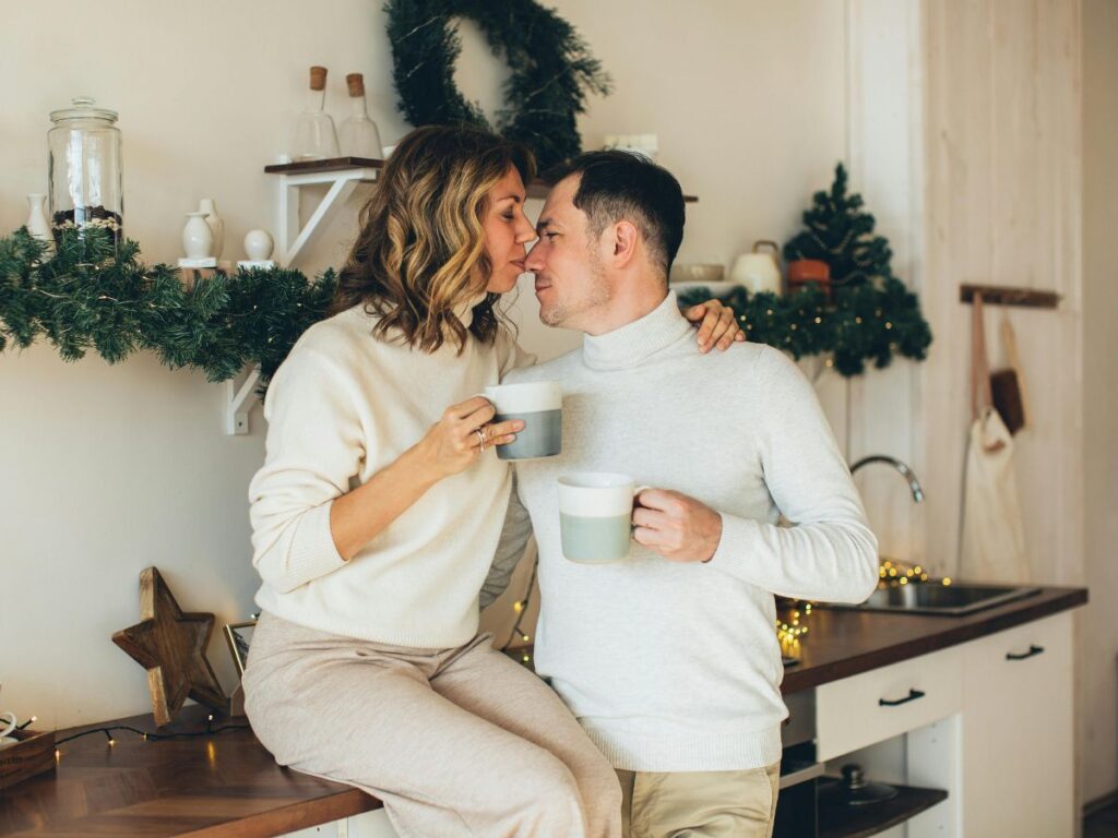 Couple sharing a cozy moment in the kitchen, holding mugs and leaning in close.