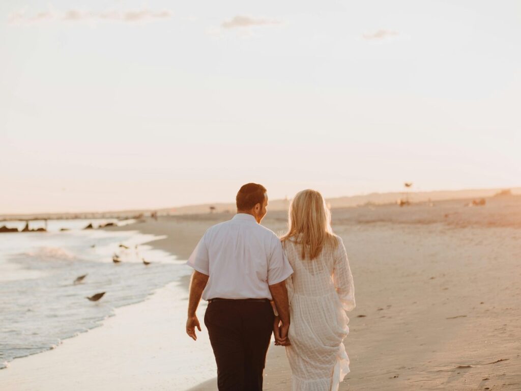 Couple holding hands while walking along the beach at sunset.