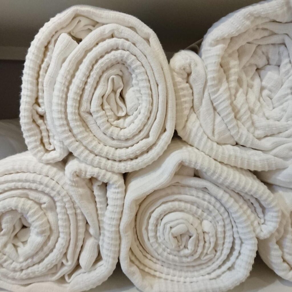 Neatly rolled white linens stacked on a shelf for organized storage.