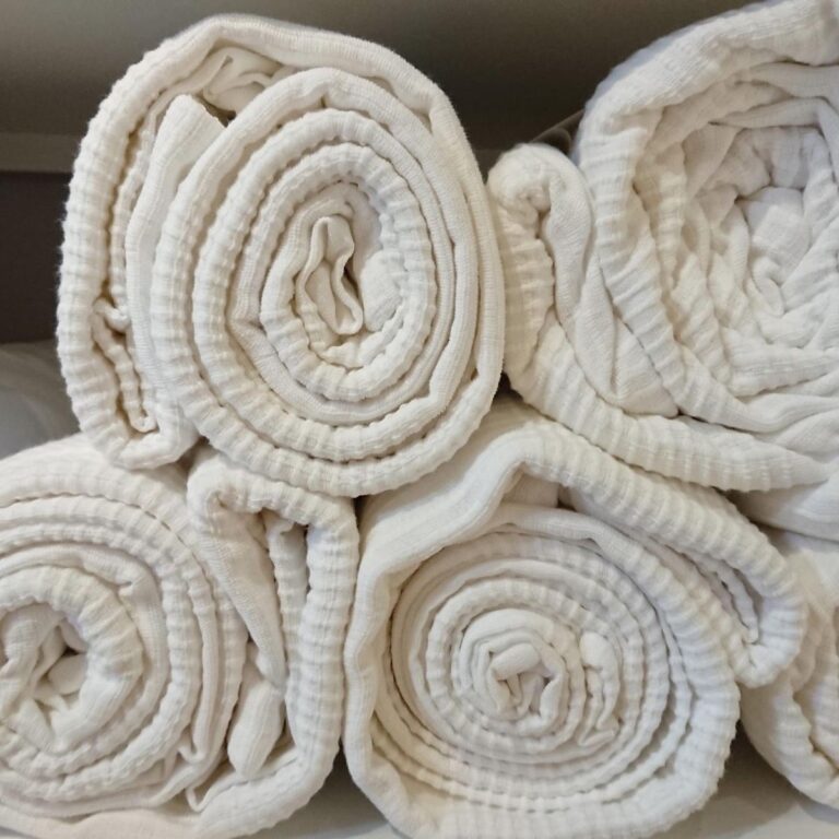 Neatly rolled white linens stacked on a shelf for organized storage.