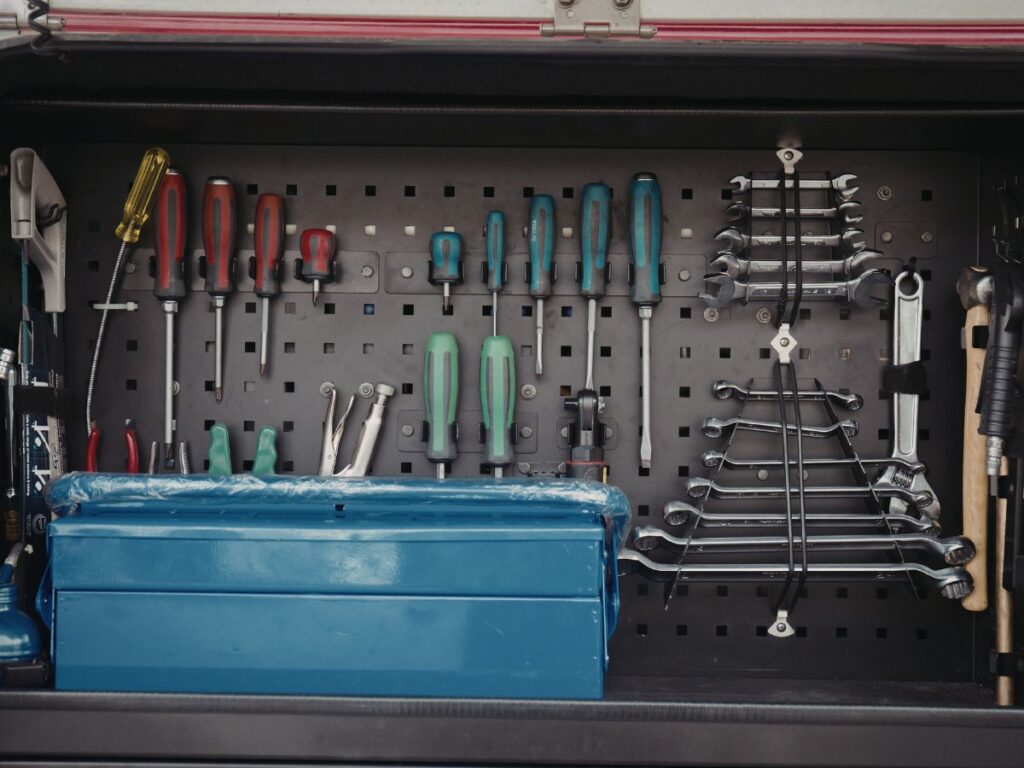 Organized tool cabinet with screwdrivers, wrenches, and a toolbox neatly arranged on a pegboard.