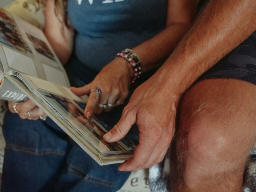 A couple sitting close together, looking through a photo album and pointing at old pictures, reminiscing over shared memories.