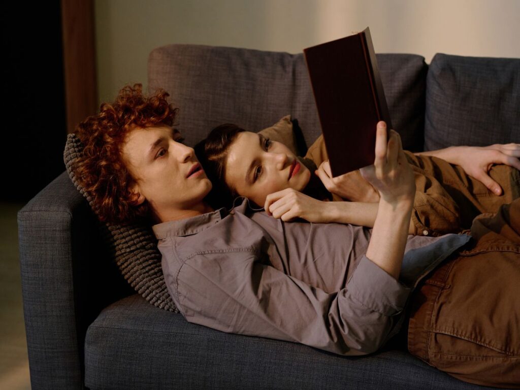 A couple lying on a couch together, reading a book and relaxing side by side.