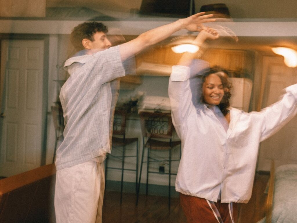 A joyful couple dancing together in their living room, smiling and spinning with carefree energy, slightly blurred to capture motion and a warm, cozy at-home vibe.
