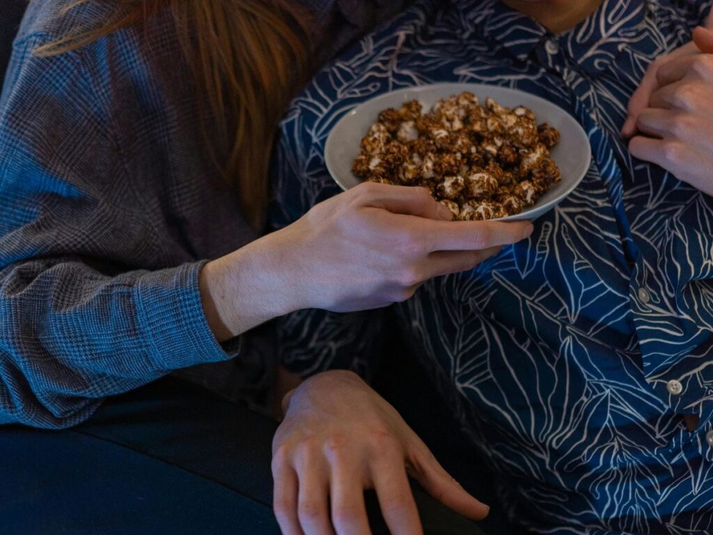 A couple sitting close together on a couch, sharing a bowl of popcorn during a cozy movie night at home.