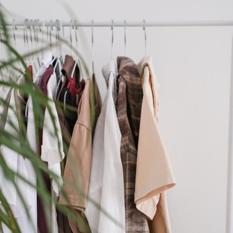 Clothing rack with neatly hung neutral-toned shirts and jackets on white hangers, arranged for an organized seasonal wardrobe rotation.